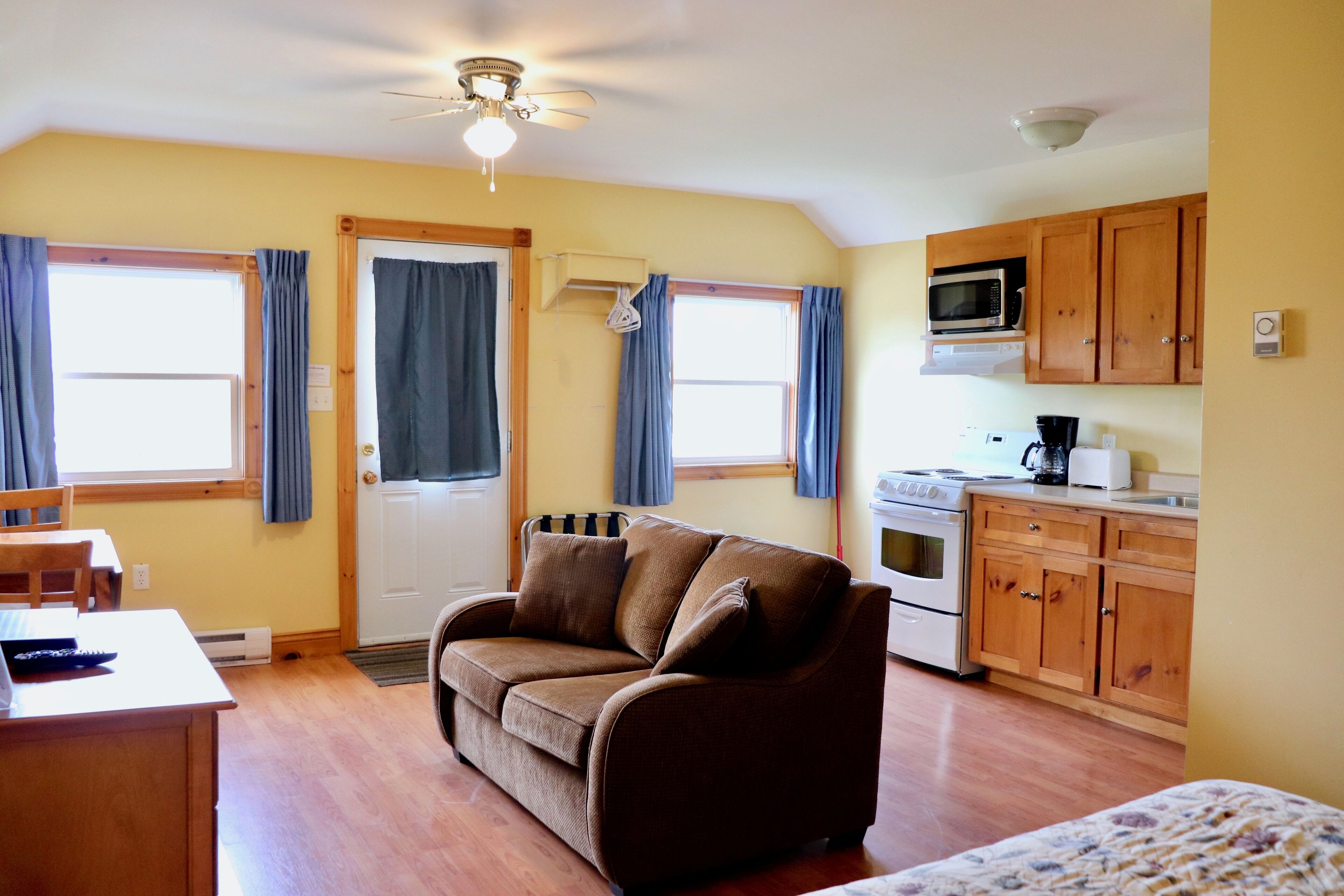 A cozy living room with a brown sofa, wooden cabinets, a microwave, and a stove.