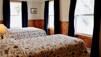 A room with two beds, wooden paneling, a window with curtains, and a framed picture on the wall.