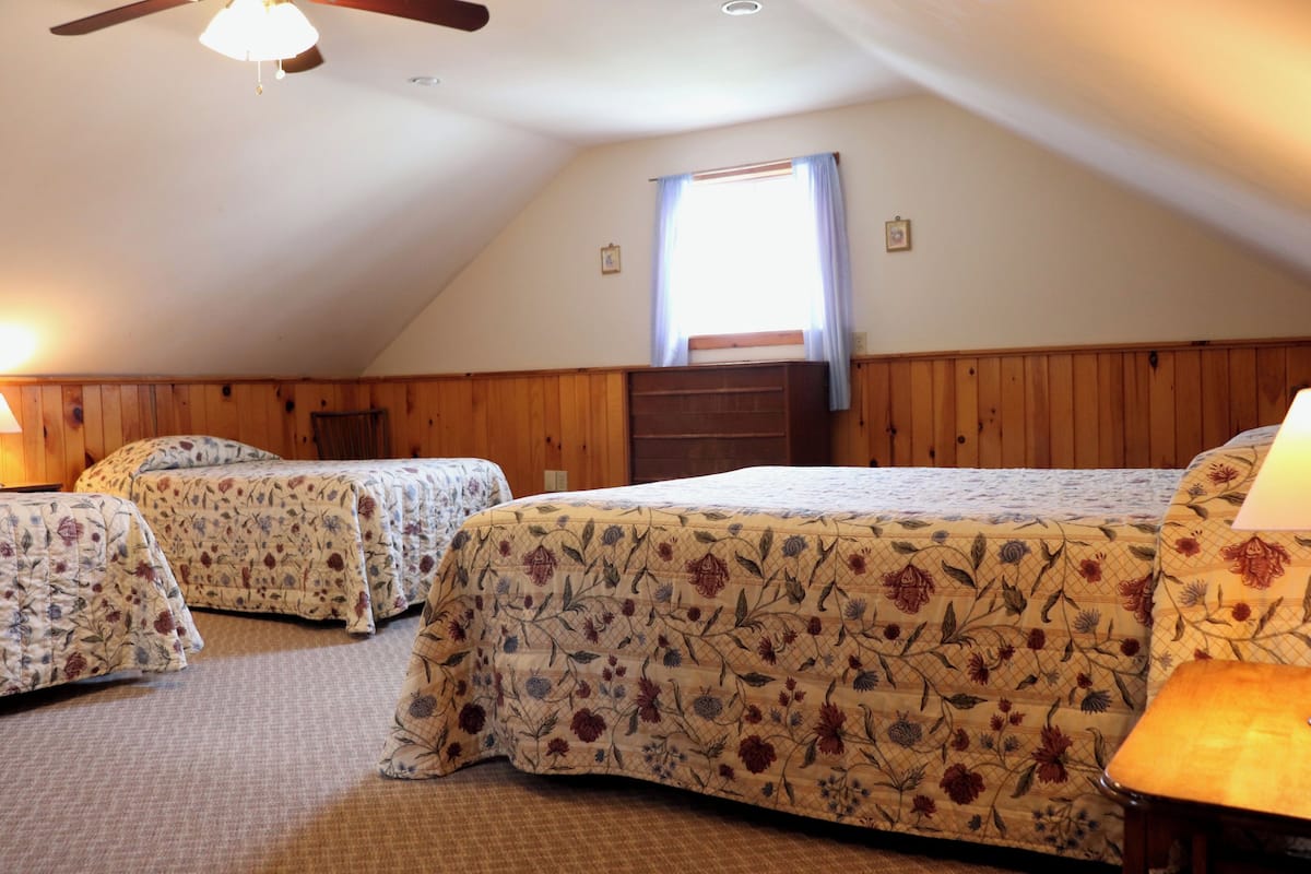 Una habitación con dos camas, paneles de madera, ventilador de techo y una ventana con cortinas.