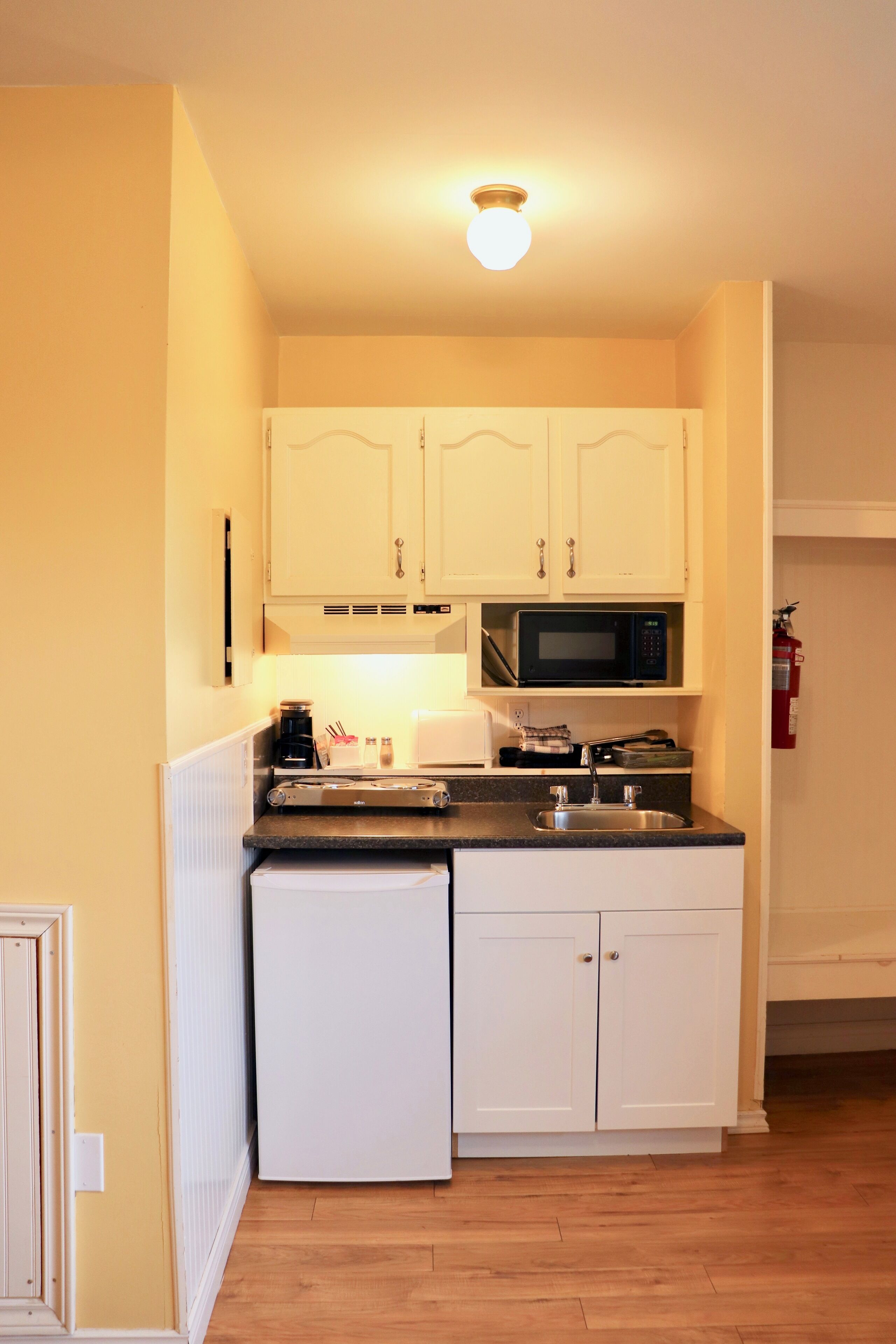 A compact kitchen with white cabinets, a microwave, a coffee maker, and a dishwasher.
