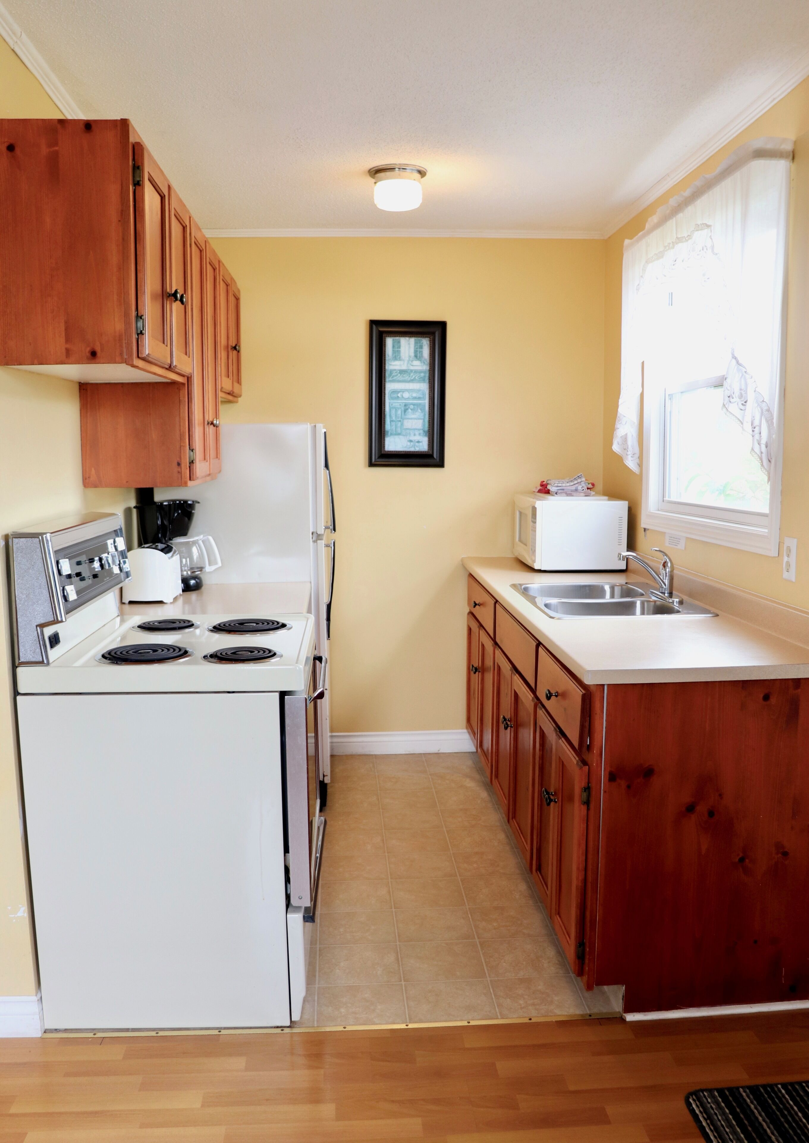 A compact kitchen with wooden cabinets, a white stove, a microwave, and a sink.