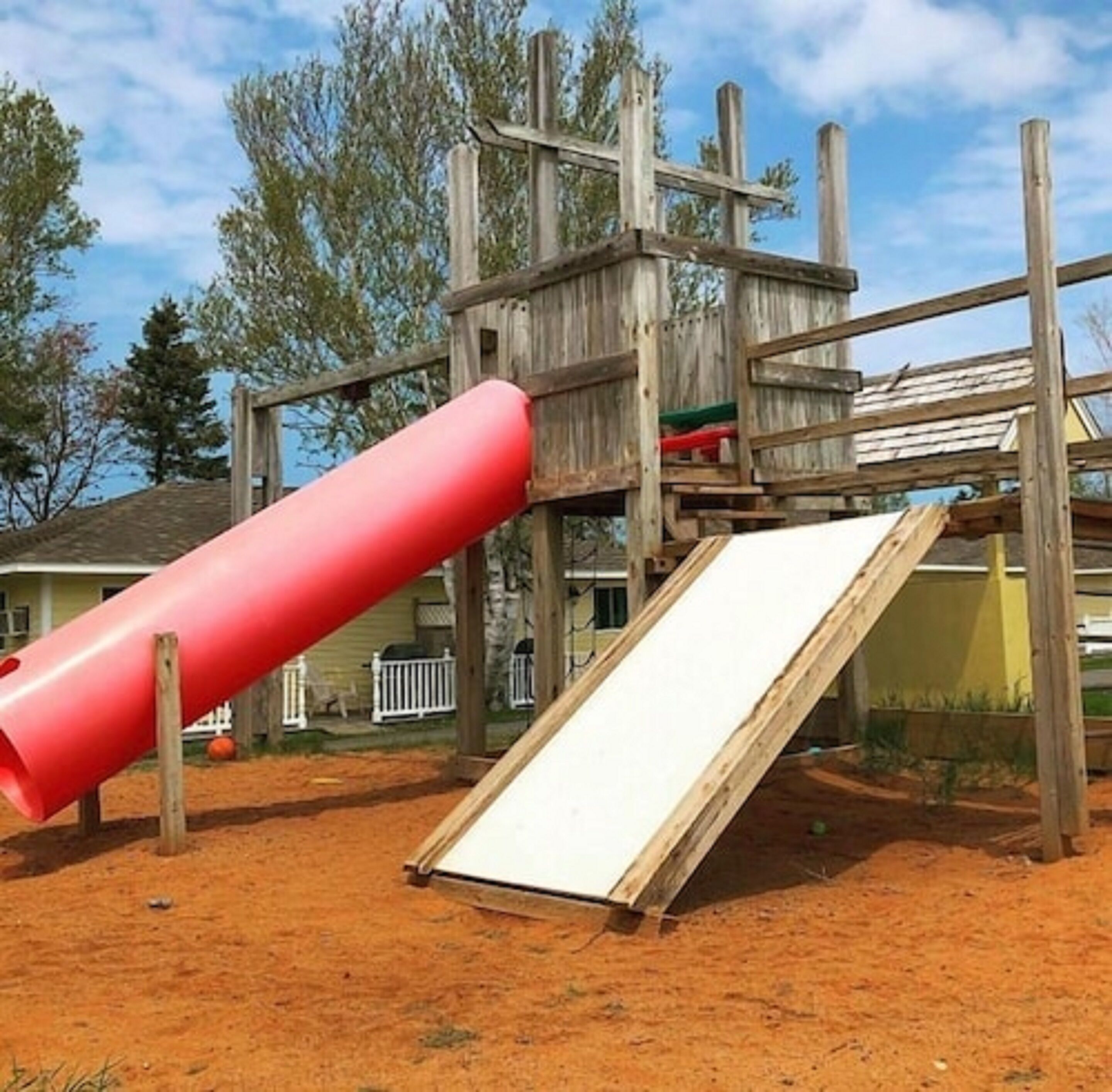 Une structure de jeu en bois avec un toboggan rouge et une rampe blanche.