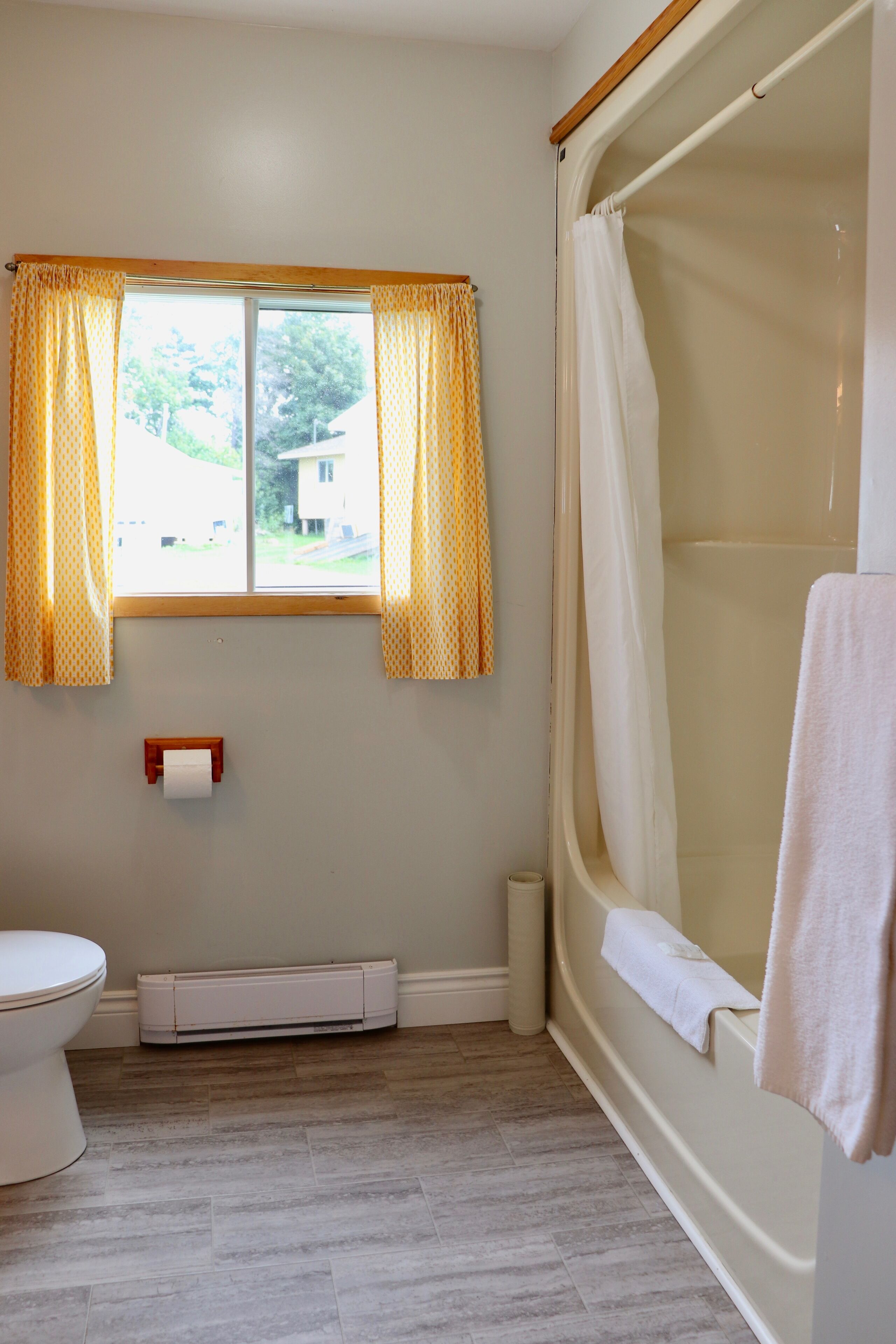 A bathroom with a toilet, a bathtub, a window with curtains, and a towel hanging on the bathtub.