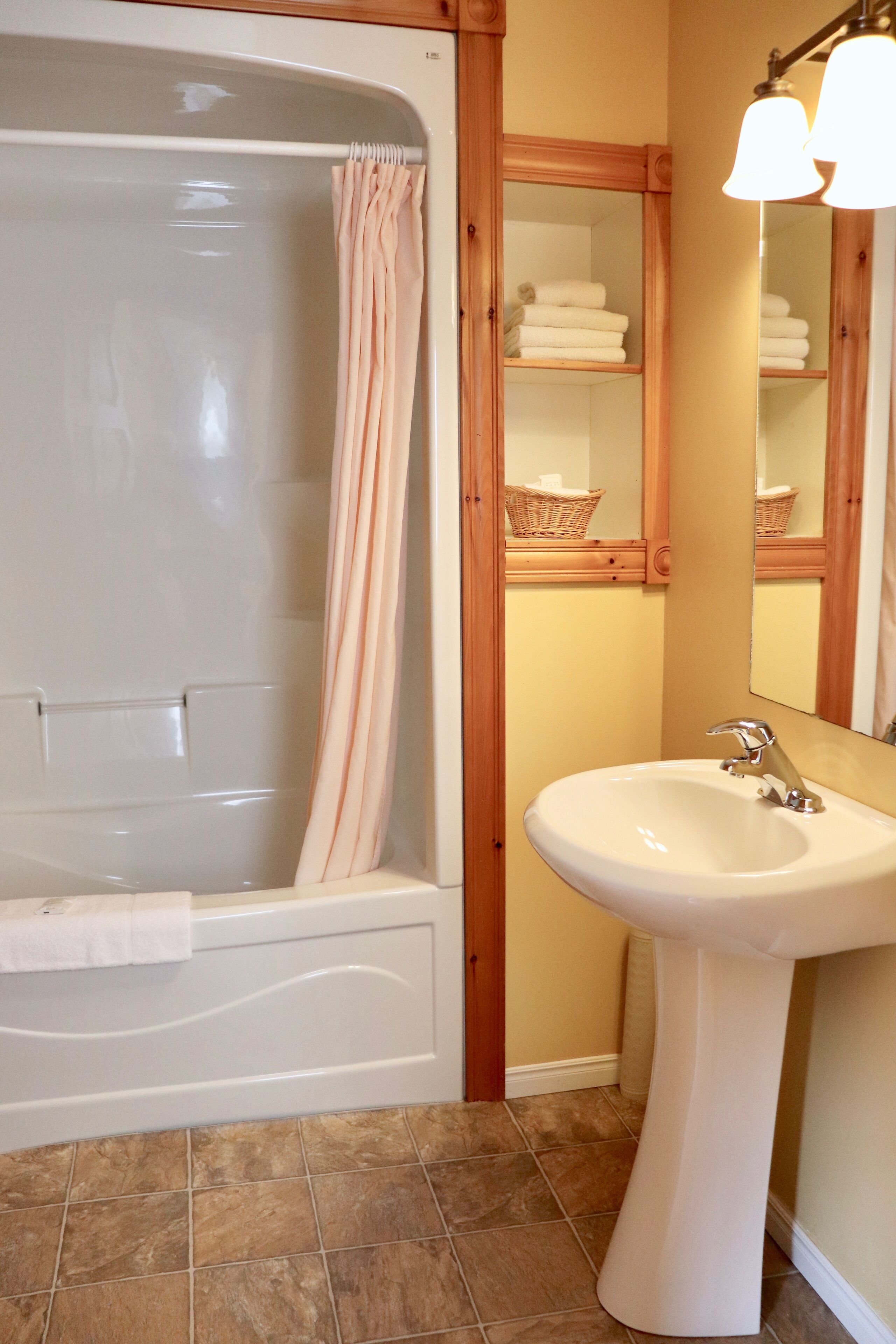 A bathroom with a bathtub, a sink, a mirror, and a shelf with towels.
