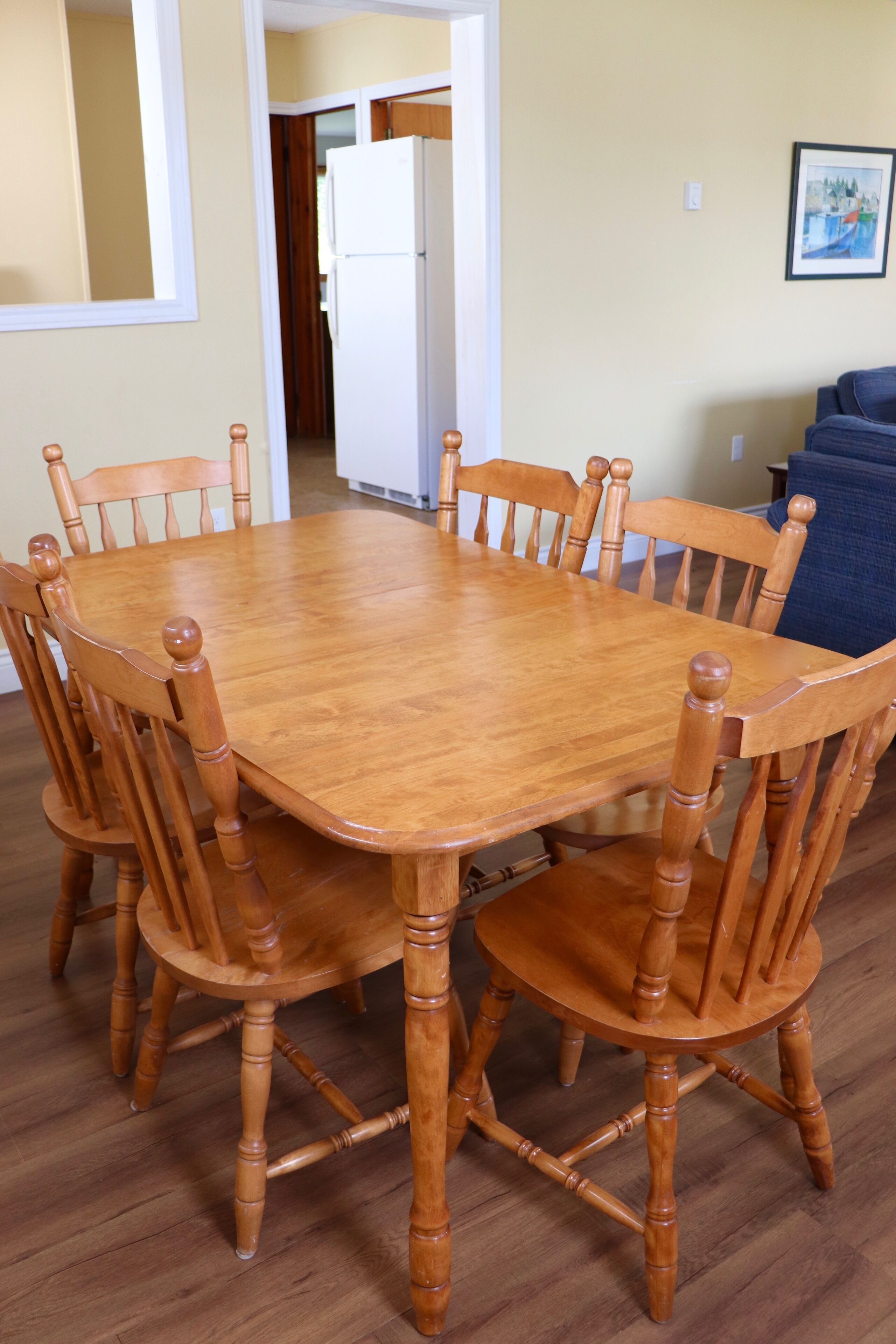 A wooden dining table surrounded by chairs in a room with a wooden floor and a door in the background.