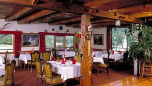 Un restaurante con vigas de madera, mesas dispuestas con manteles blancos y servilletas rojas.