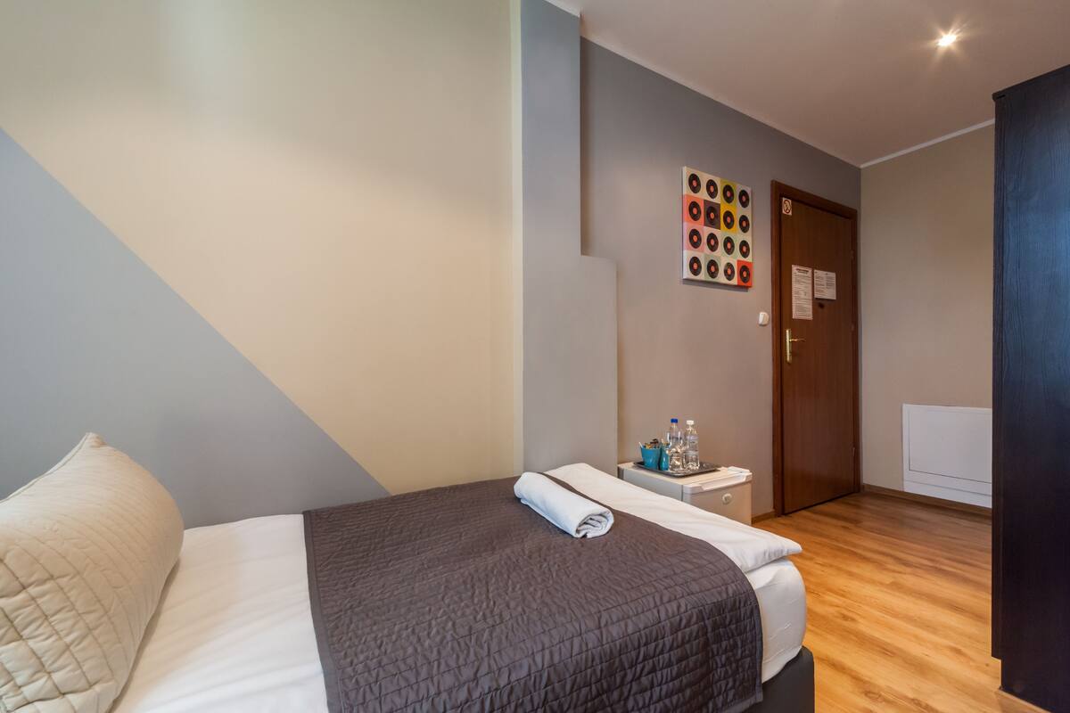 A hotel room with a bed, a nightstand, a wall art piece, and a door.
