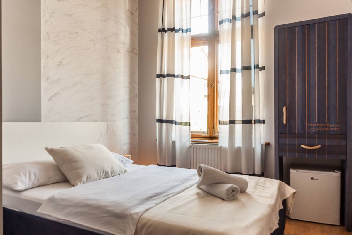 A hotel room with a bed, a small bedside table, a radiator, and a wardrobe.