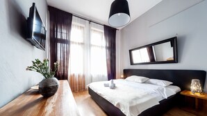 Et moderne hotelværelse med en stor seng, et fladskærms-tv på væggen, et sengebord med en lampe og et vindue med gardiner.