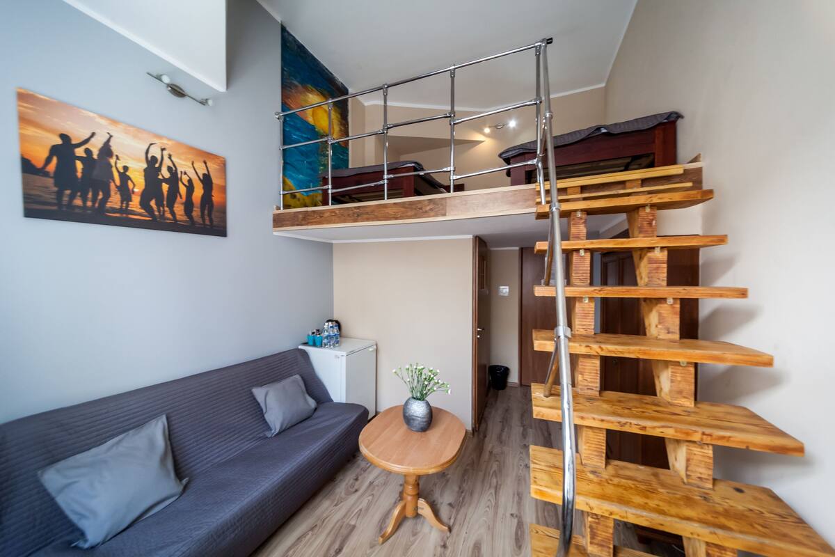 A modern loft-style room with a grey sofa, a small wooden table, and a wooden staircase.
