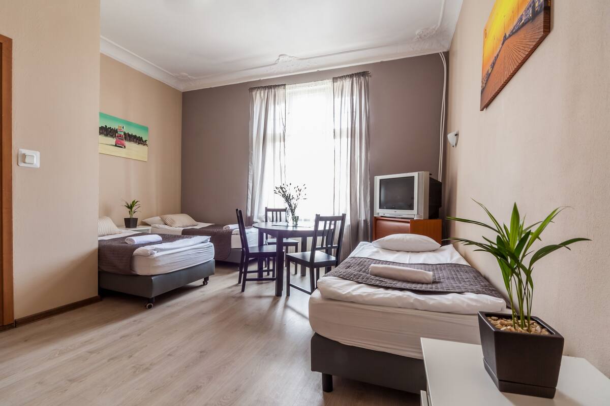 A hotel room with two beds, a dining table, a TV, and a potted plant.