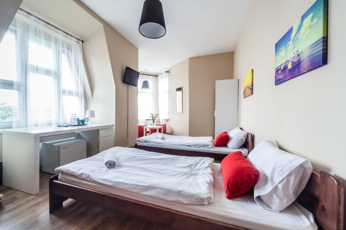 A hotel room with two beds, a desk, a chair, a TV, and a window with curtains.