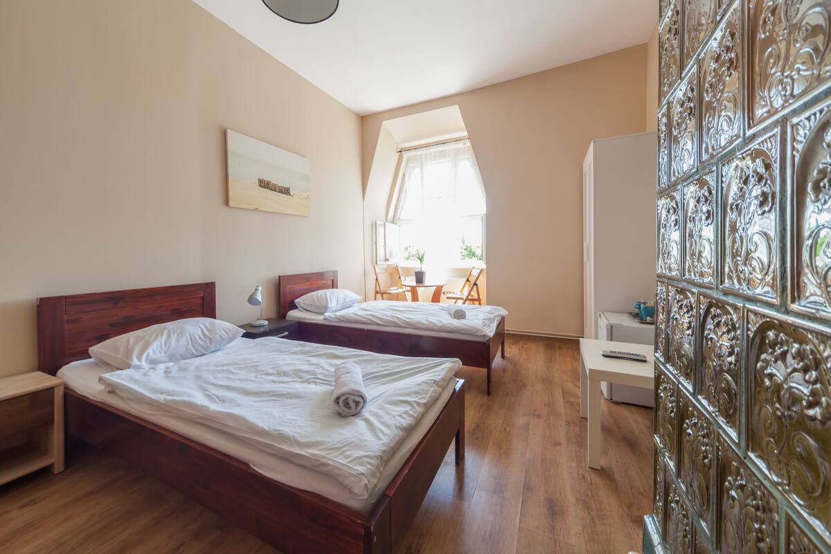 A hotel room with two wooden beds, a small table, and a window with ornate metal grilles.