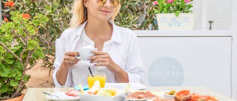 A person sitting at a table with a meal consisting of fruits, bread, and a drink.