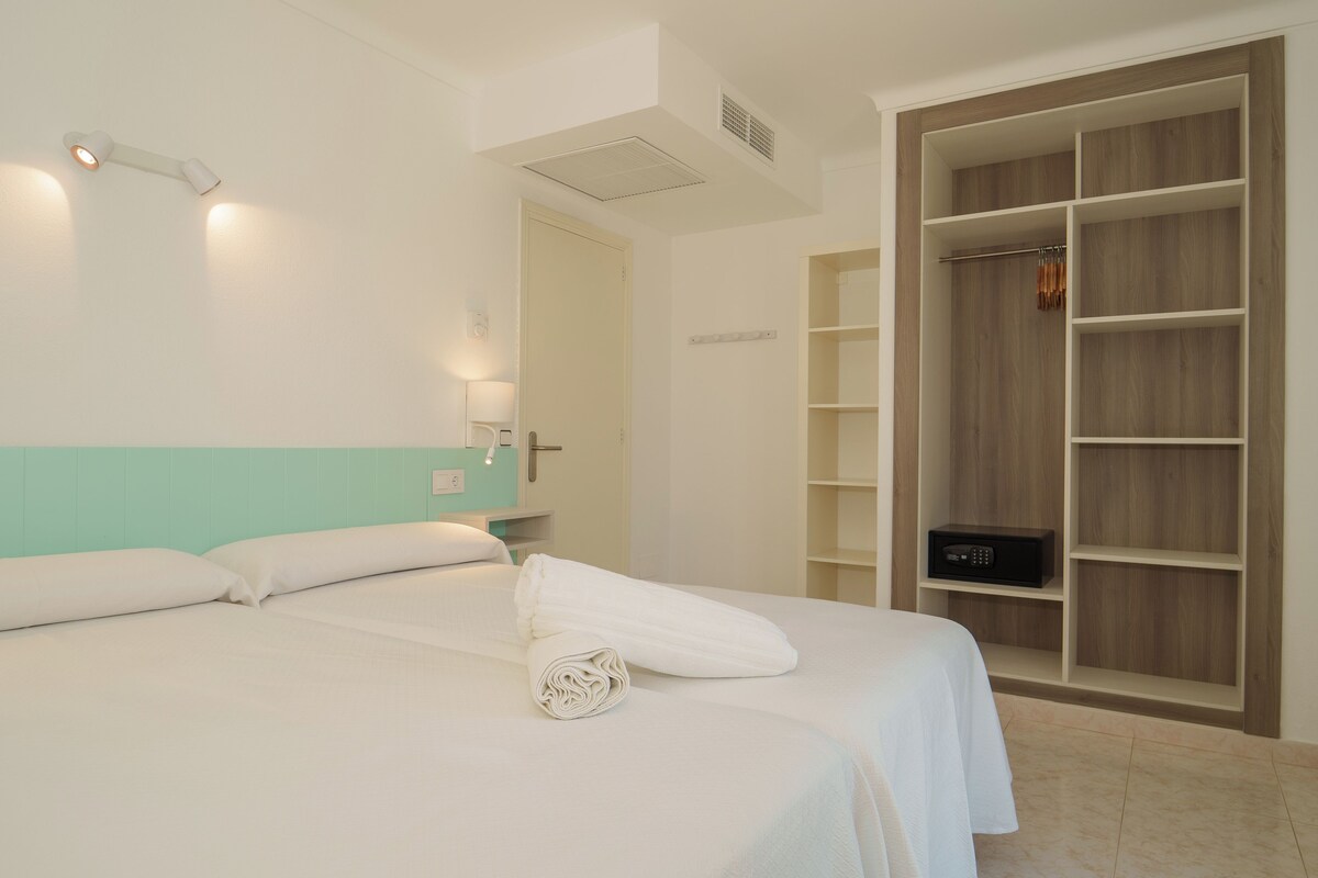 Habitació d'hotel amb llit, un armari i una taula petita amb làmpada.