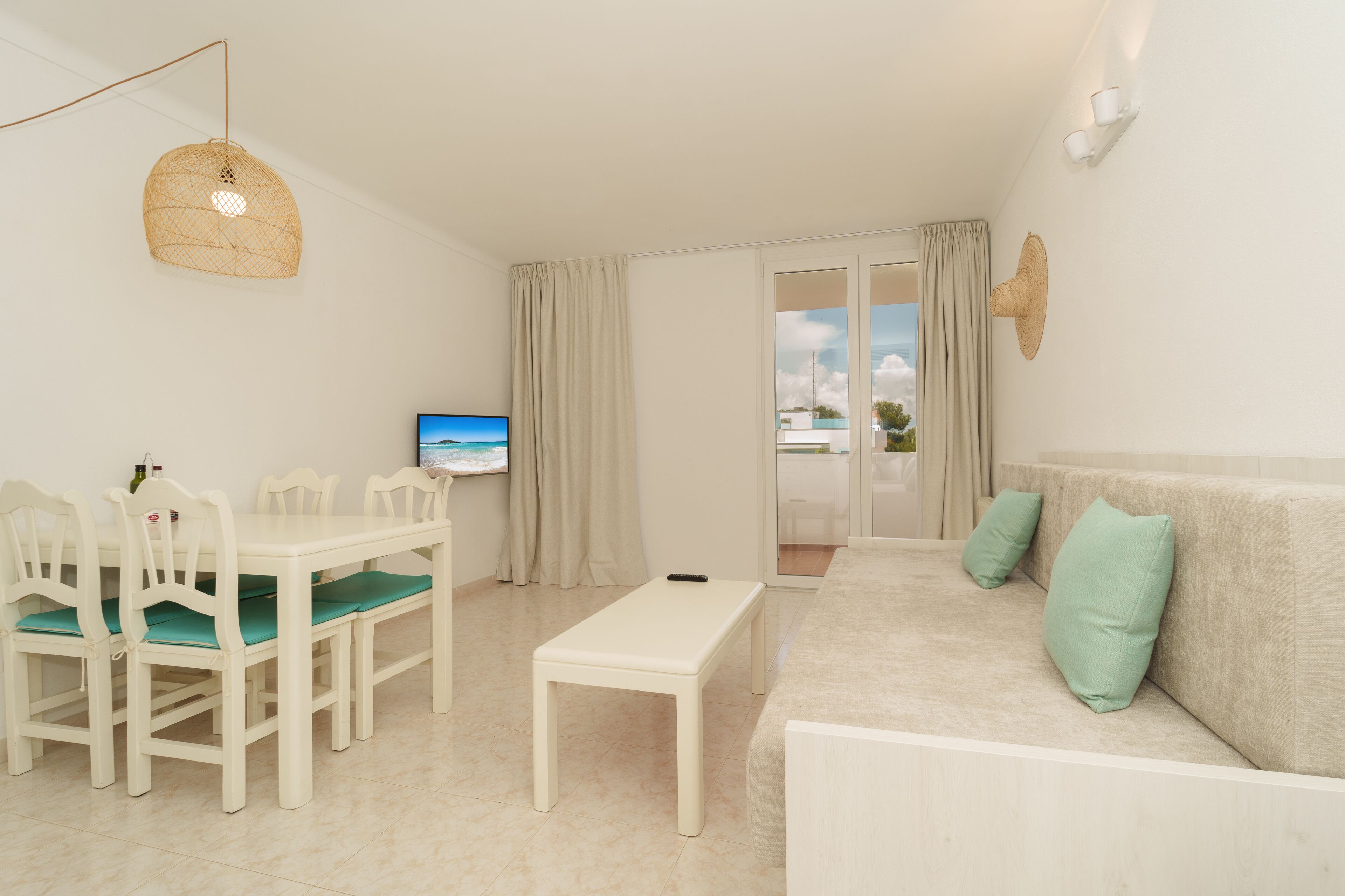 A modern living room with a dining area, a sofa with cushions, a television, and a view through the glass door.