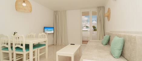 A modern living room with a dining area, a sofa with cushions, a television, and a view through the glass door.
