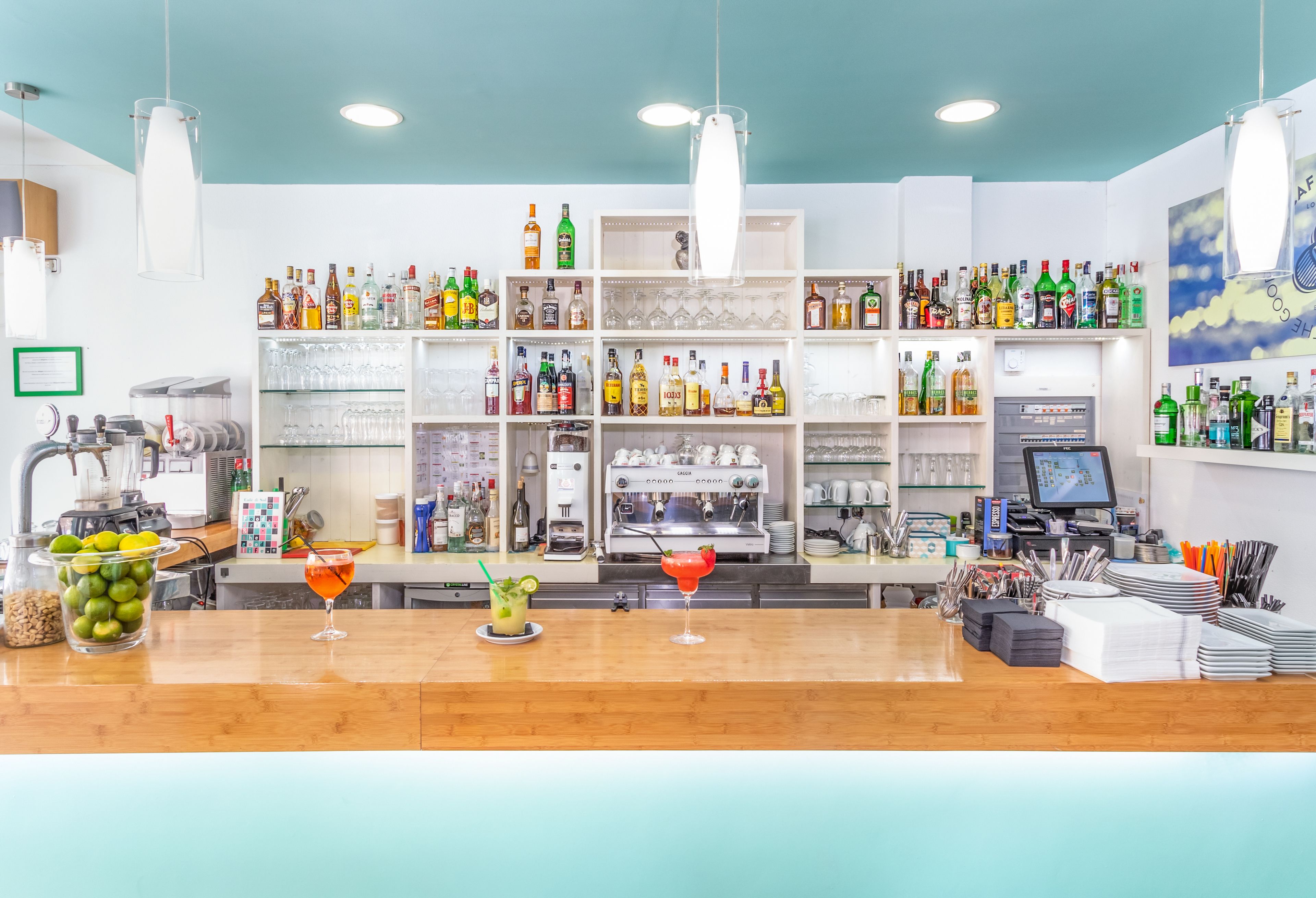 A bar area with shelves of liquor bottles, a coffee machine, and a counter with glasses and a cocktail.