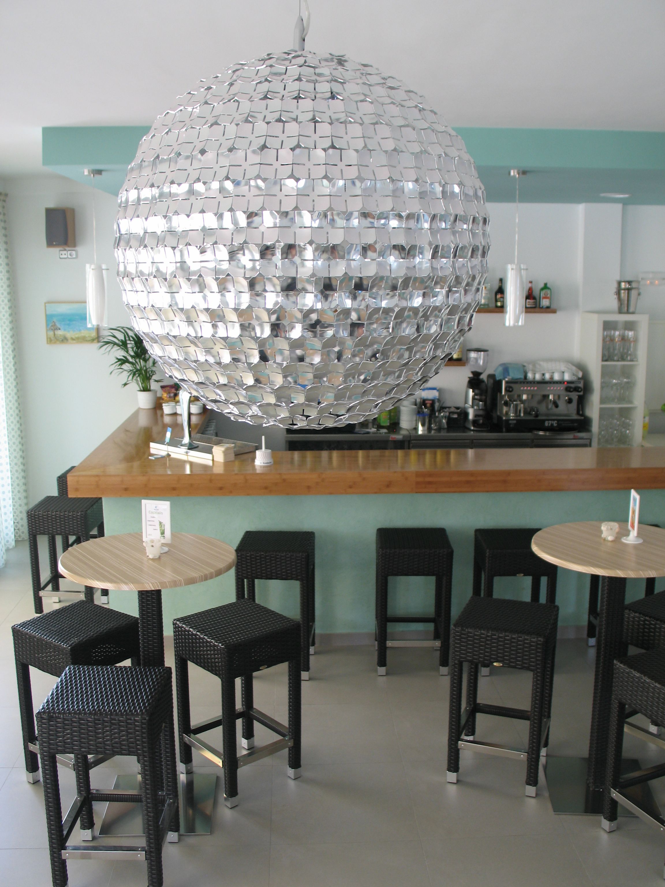 Un espace bar doté d’une grande boule à facettes, de chaises en osier noir et d’un comptoir en bois.