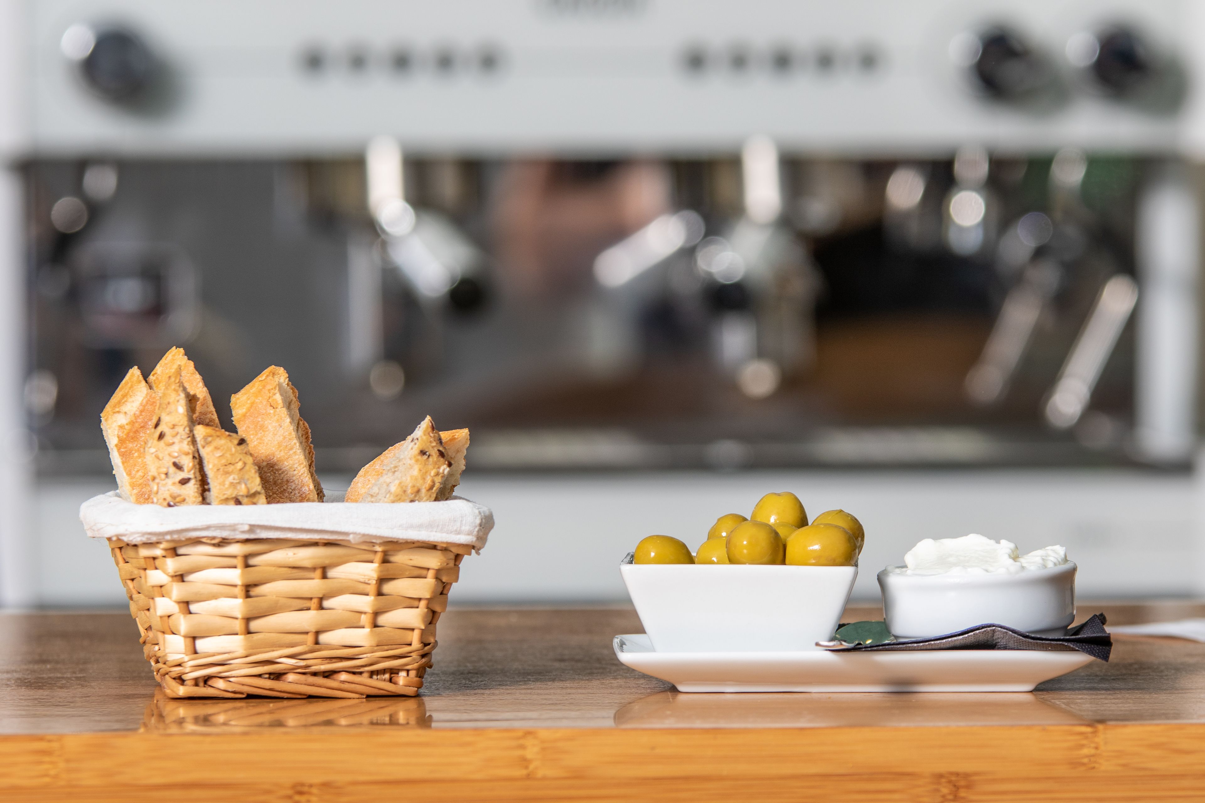 A kitchen counter with a basket of bread, a bowl of olives, and a bowl of cream cheese.