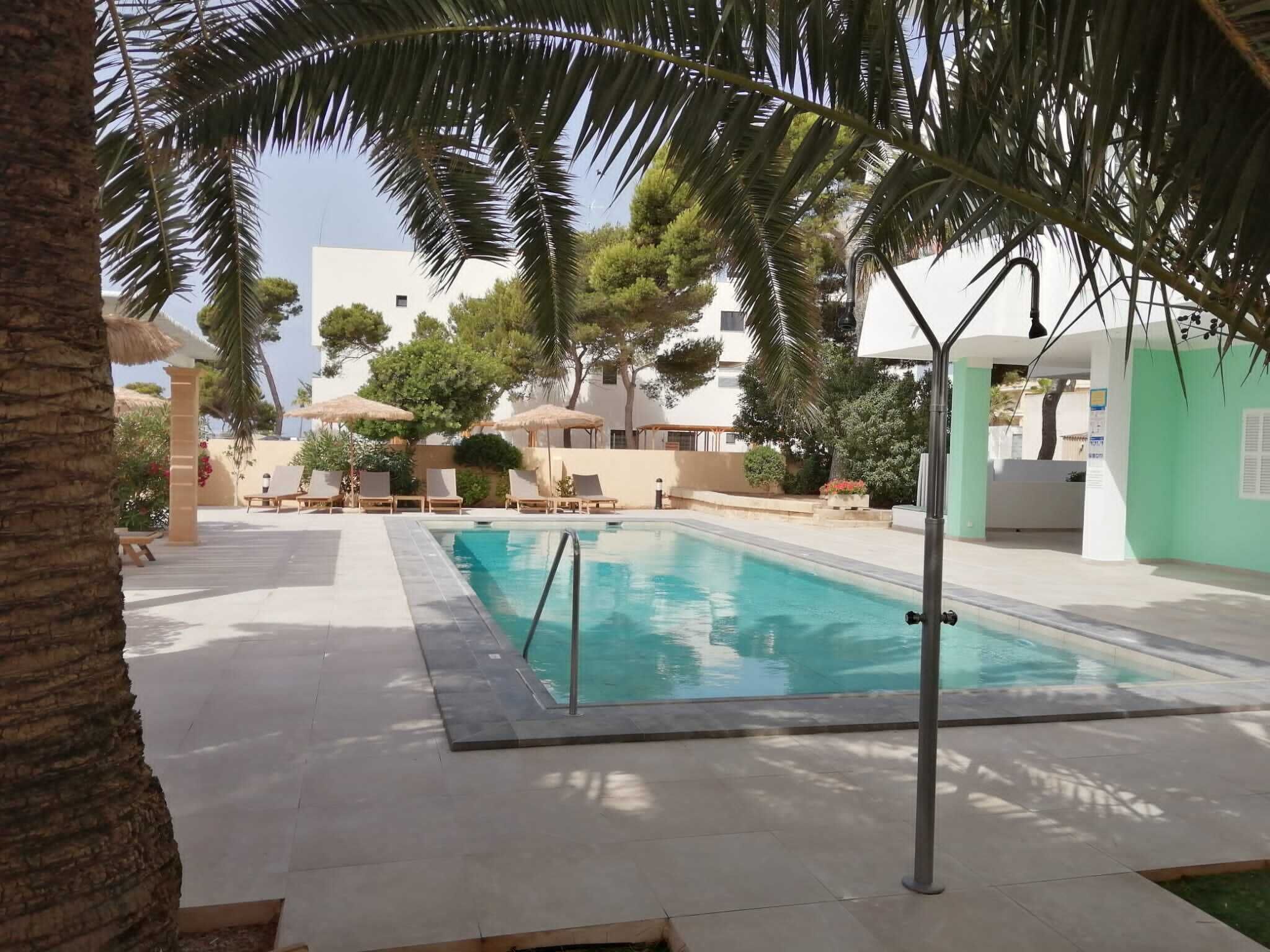 A swimming pool with lounge chairs and umbrellas, surrounded by palm trees and buildings.
