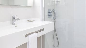 Un baño moderno con ducha envuelta en vidrio, un tocador blanco con espejo y una toalla colgada en un perchero.