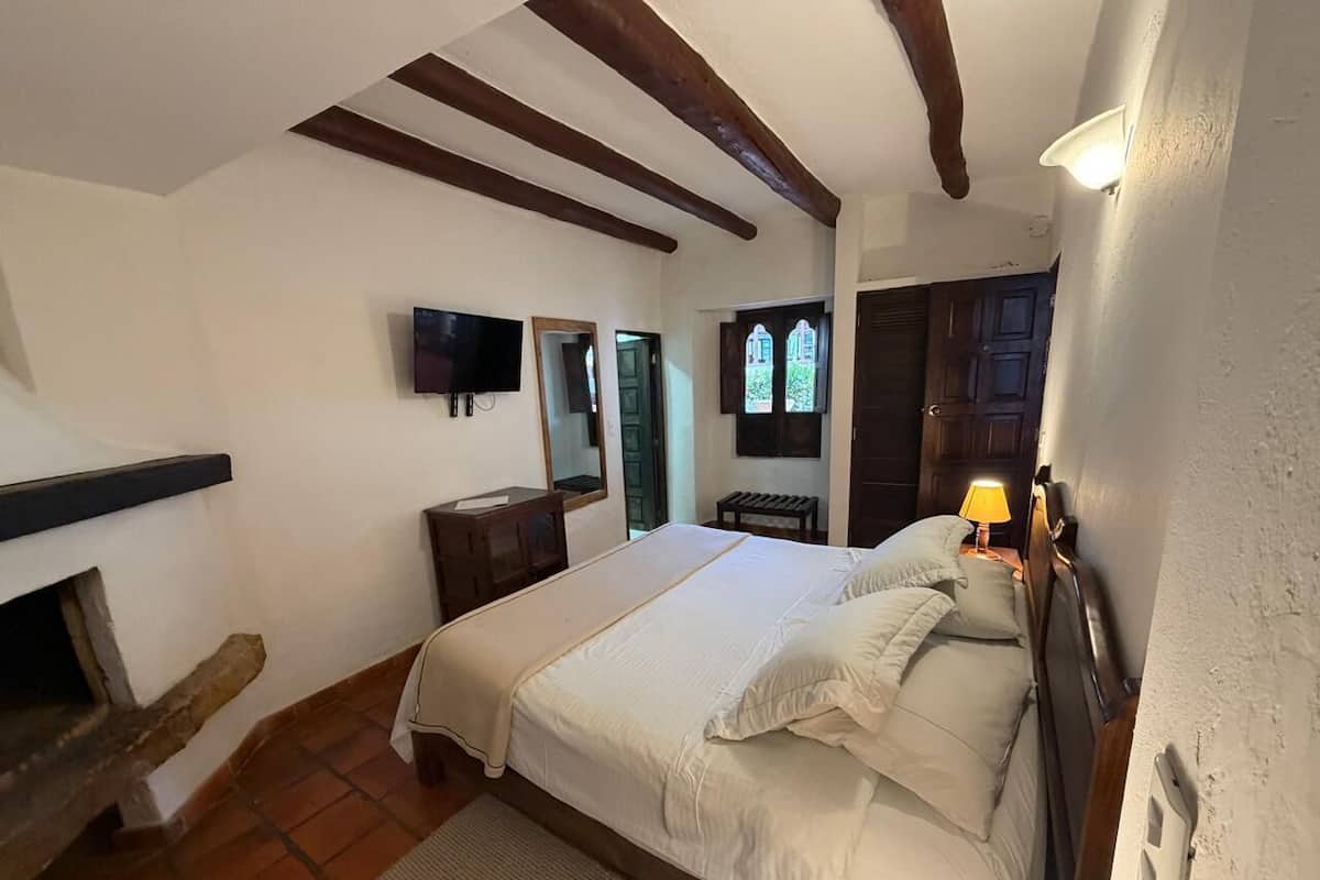 Een slaapkamer met een bed, een televisie, een houten bankje, een klein tafeltje en een raam met uitzicht.