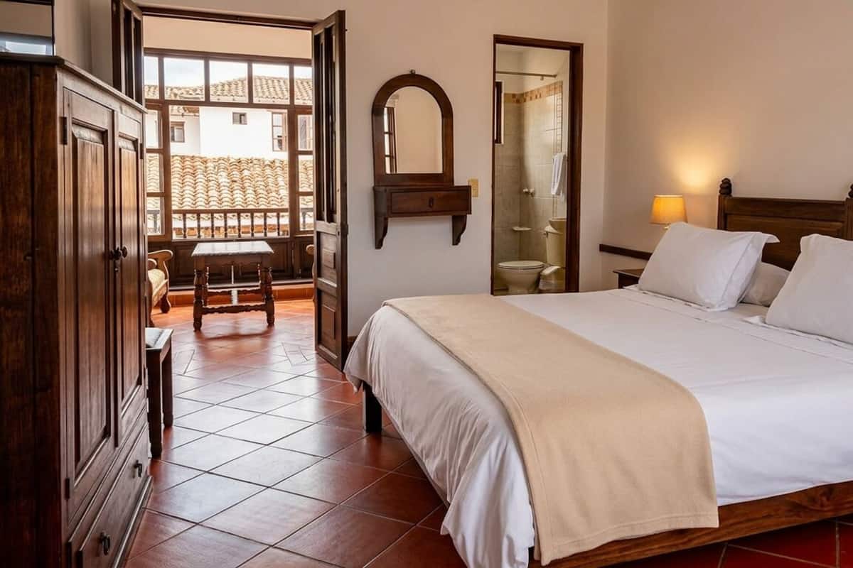 Een hotelkamer met een bed, een houten kledingkast, een spiegel, een badkamer met douche en uitzicht op het exterieur.