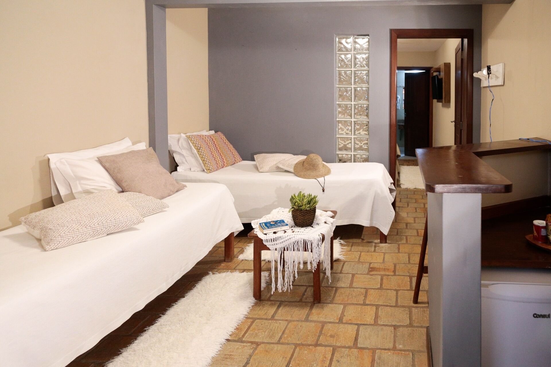 A hotel room with two beds, a small table with a plant, a white rug, and a desk with a chair.