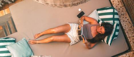 A person lying on a bed with striped pillows, a smartphone, and a book.