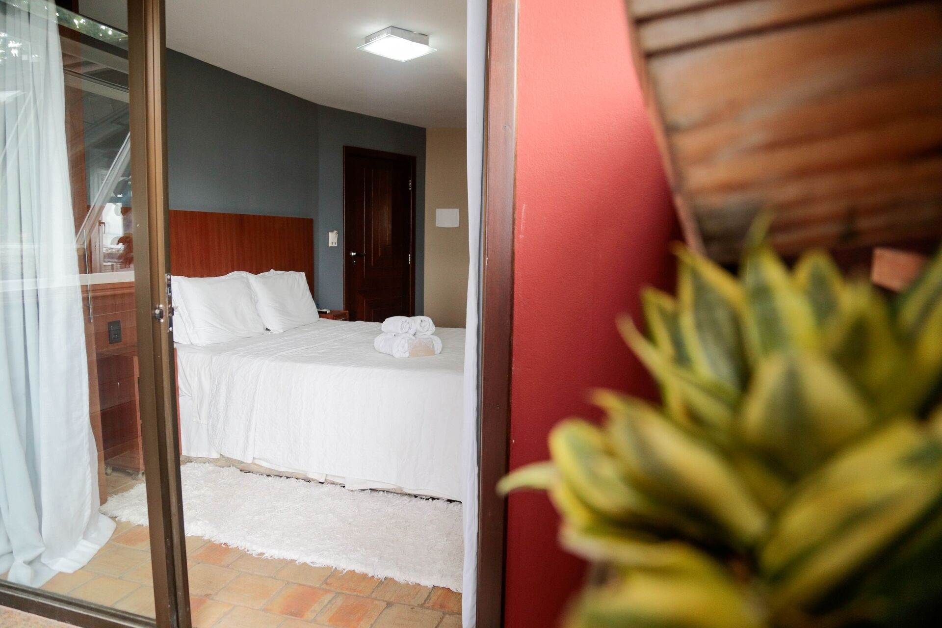 Een hotelkamer met een bed, een houten hoofdbord, een zacht, wit tapijt en een plant in pot.