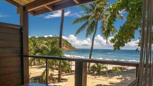Un hamac sur une terrasse en bois donnant sur une plage bordée de palmiers et sur l’océan.