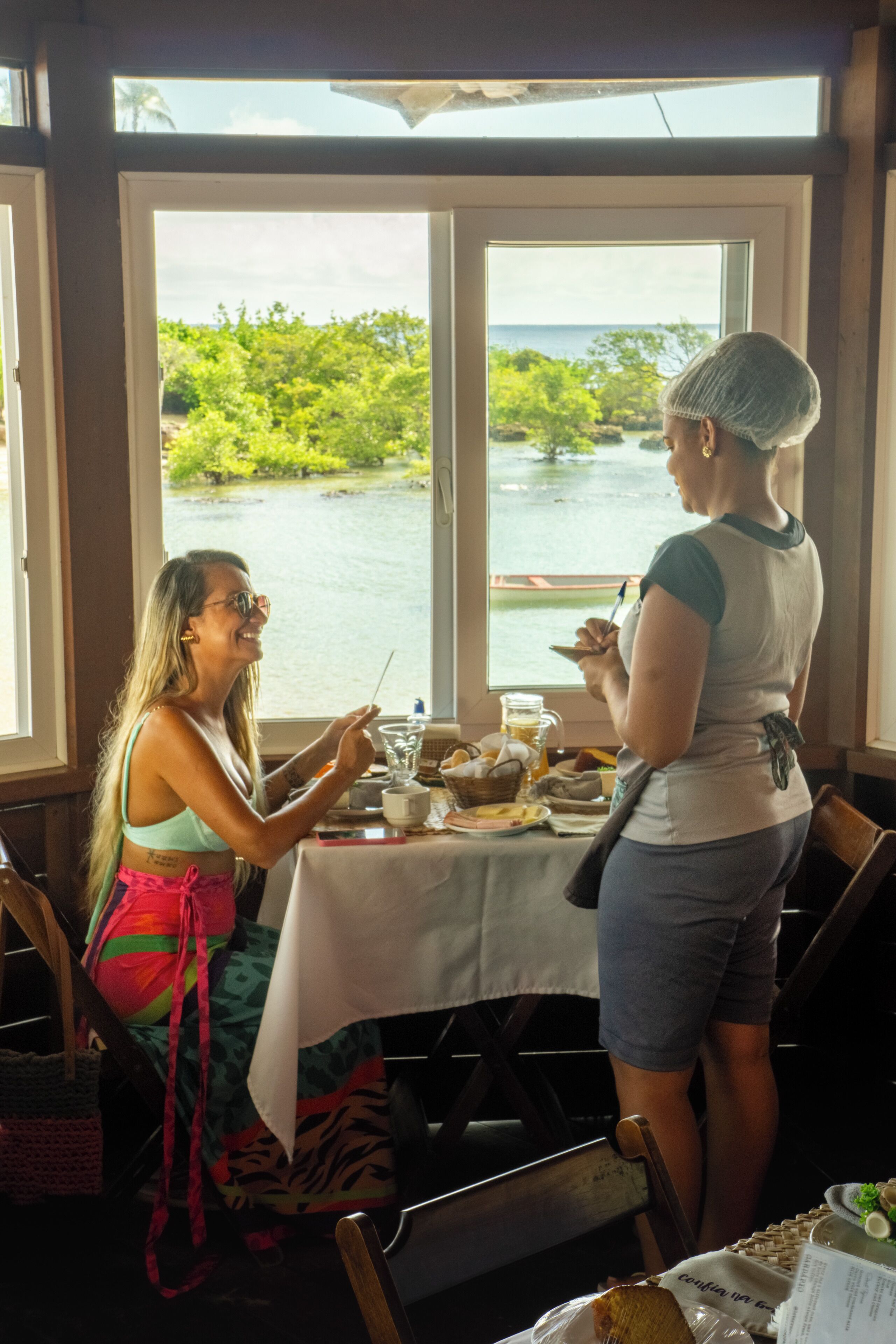 Two people dining at a table with a view of a body of water and greenery.