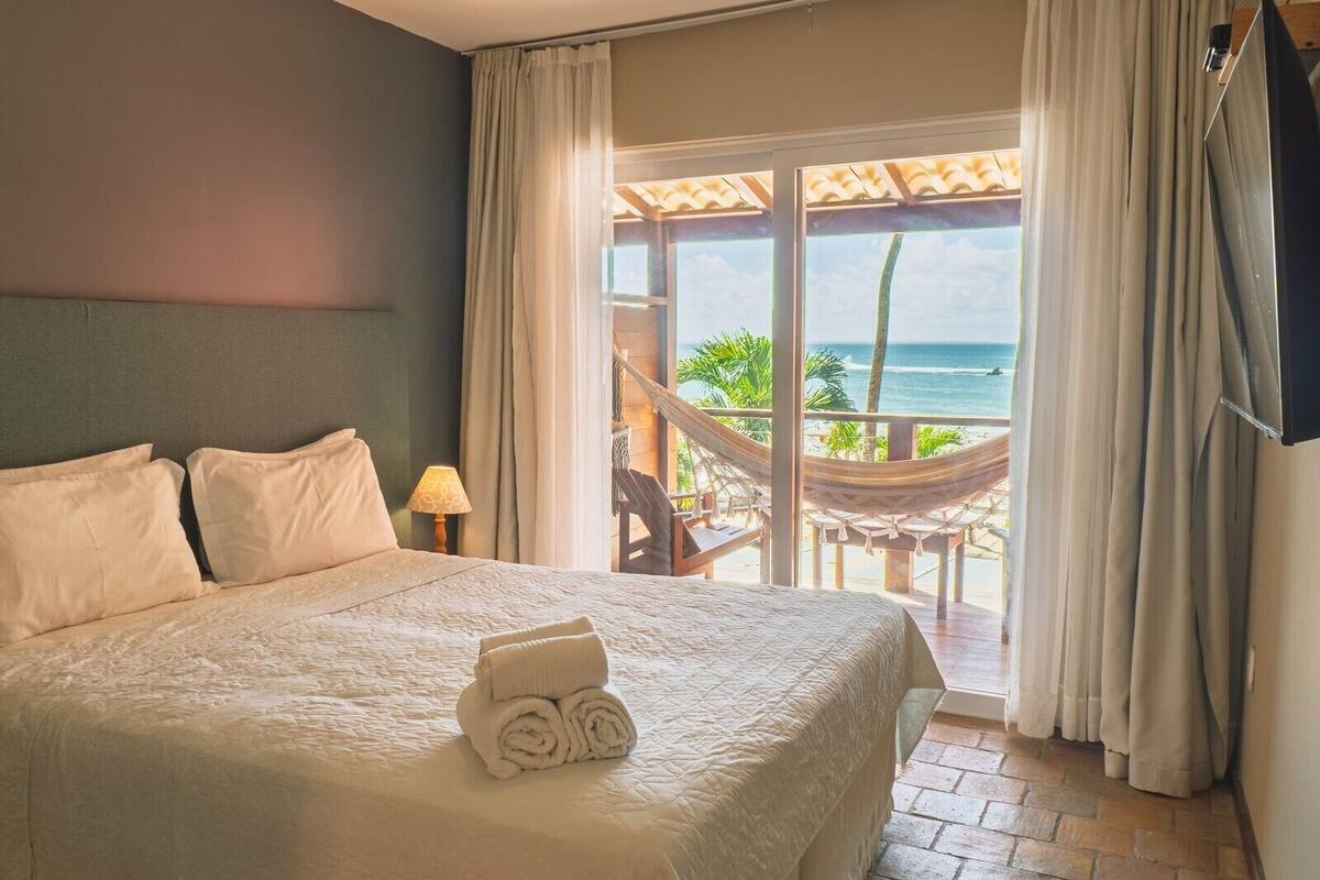 Une chambre d’hôtel avec un lit, une vue sur l’océan, un hamac et un téléviseur fixé au mur.