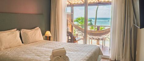 A hotel room with a bed, a view of the ocean, a hammock, and a TV mounted on the wall.
