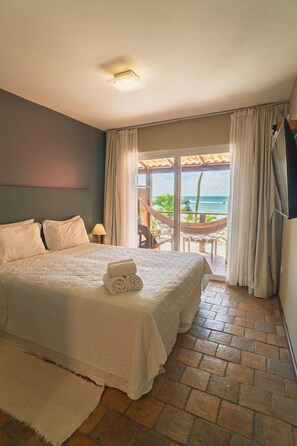 Een hotelkamer met een bed, uitzicht op zee, een hangmat en een aan de muur bevestigde televisie.