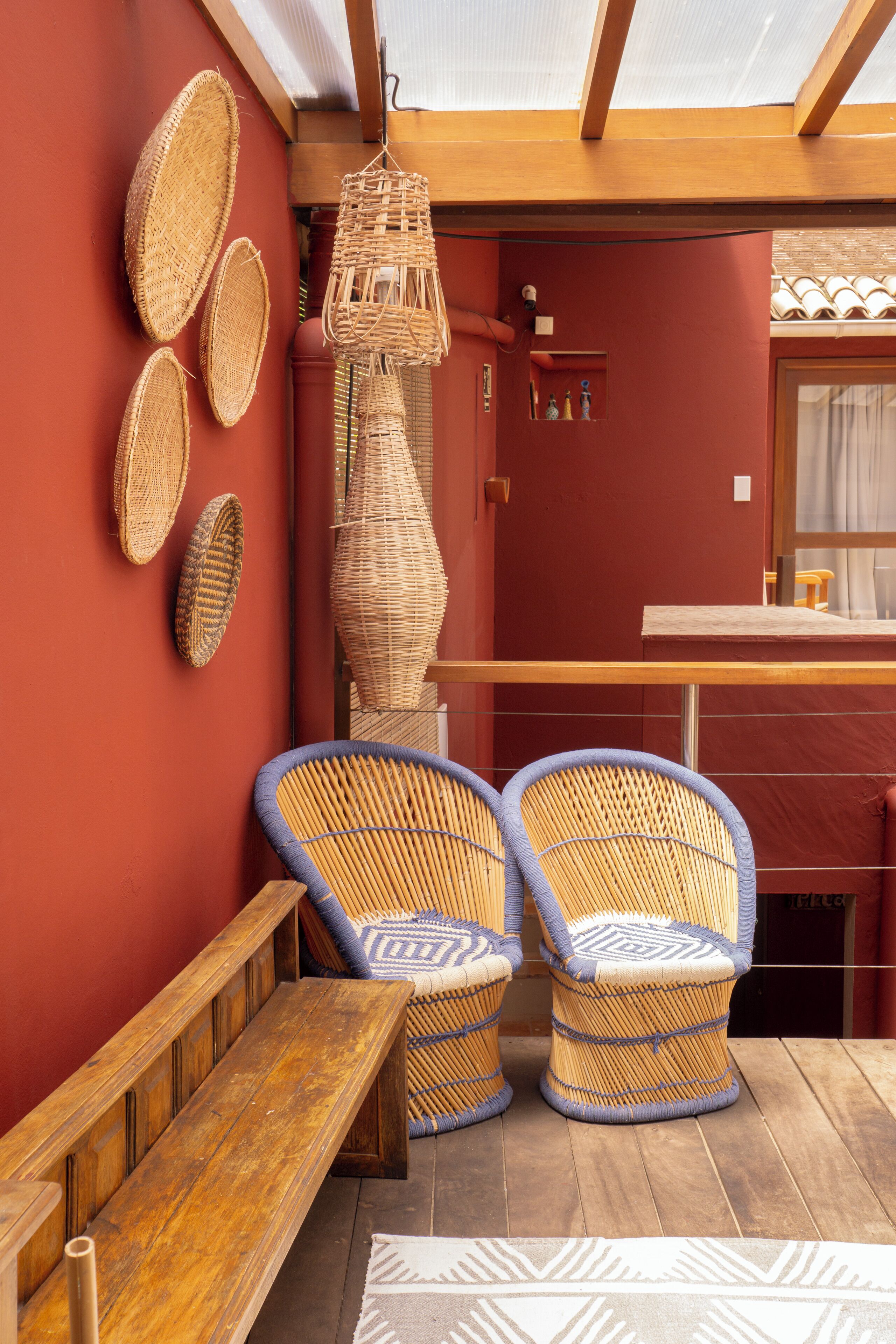 A room with a wooden bench, two wicker chairs, and a hanging wicker lamp.