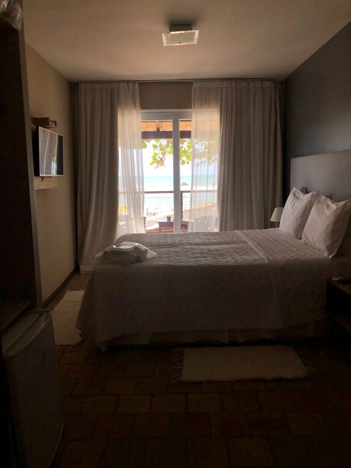 A bedroom with a bed, curtains, a TV, and a view of the beach.