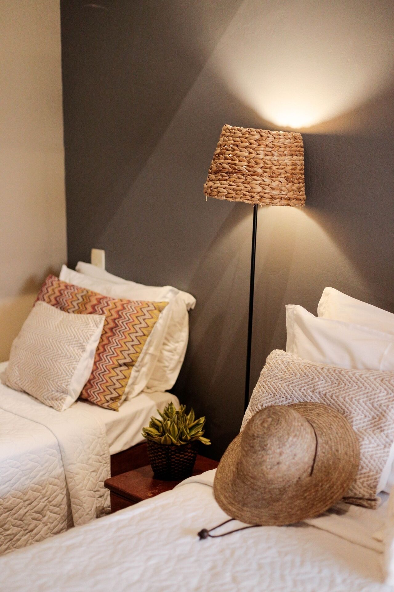 A neatly arranged bedroom with a bed, pillows, a floor lamp, and a small potted plant.