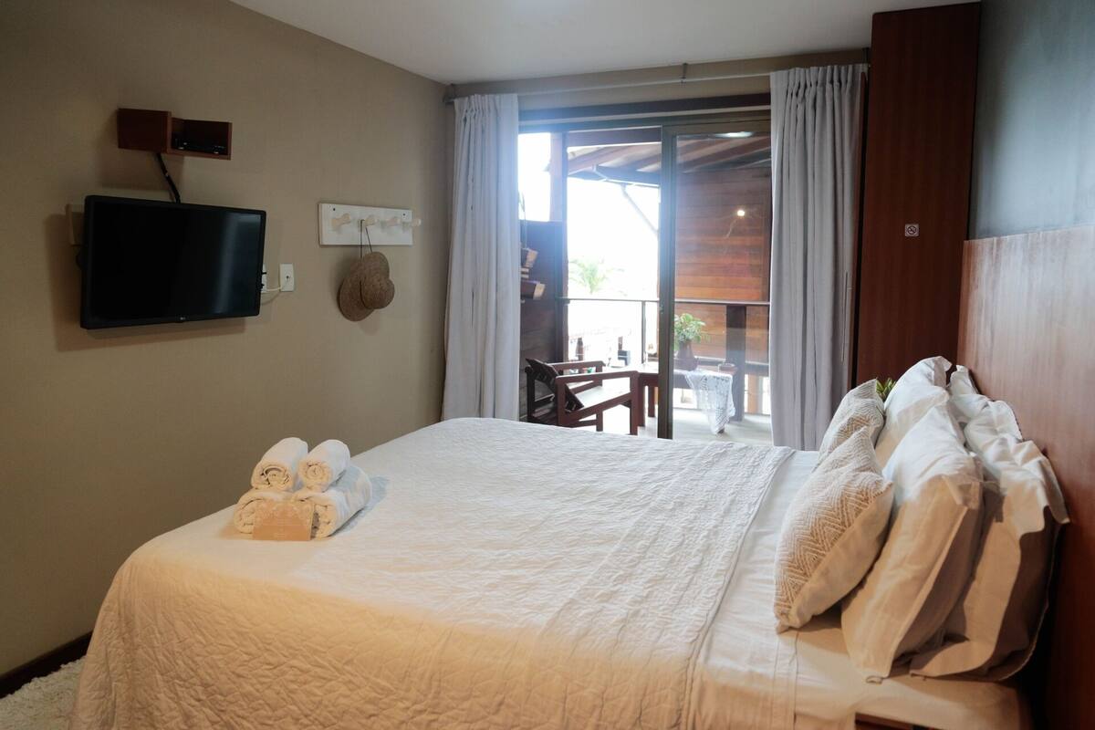 Une chambre d’hôtel avec un lit, un téléviseur fixé au mur, une petite table et une vue sur l’extérieur grâce à une porte coulissante.