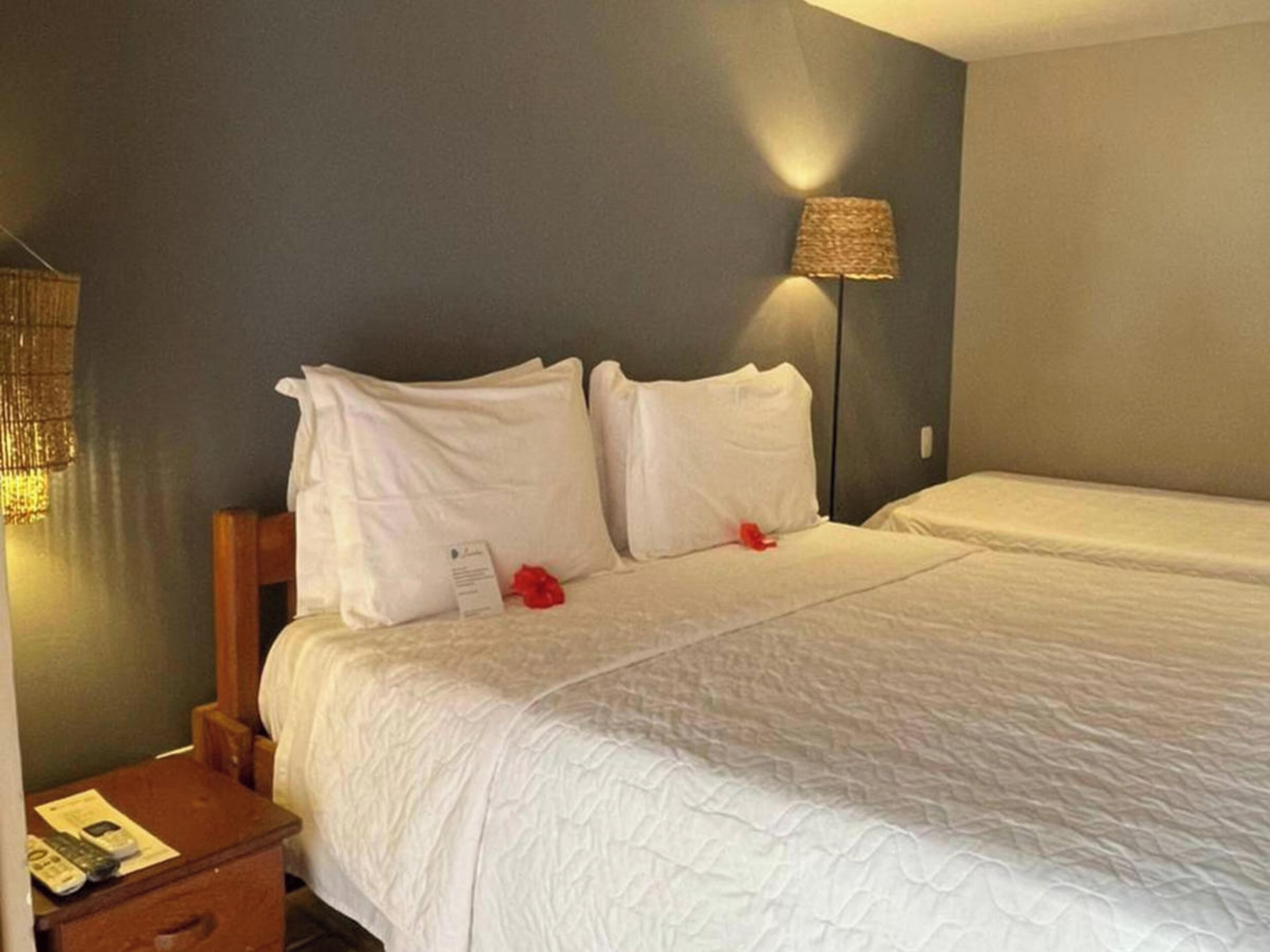 A hotel room with a bed, a nightstand, a lamp, and a wall-mounted light fixture.