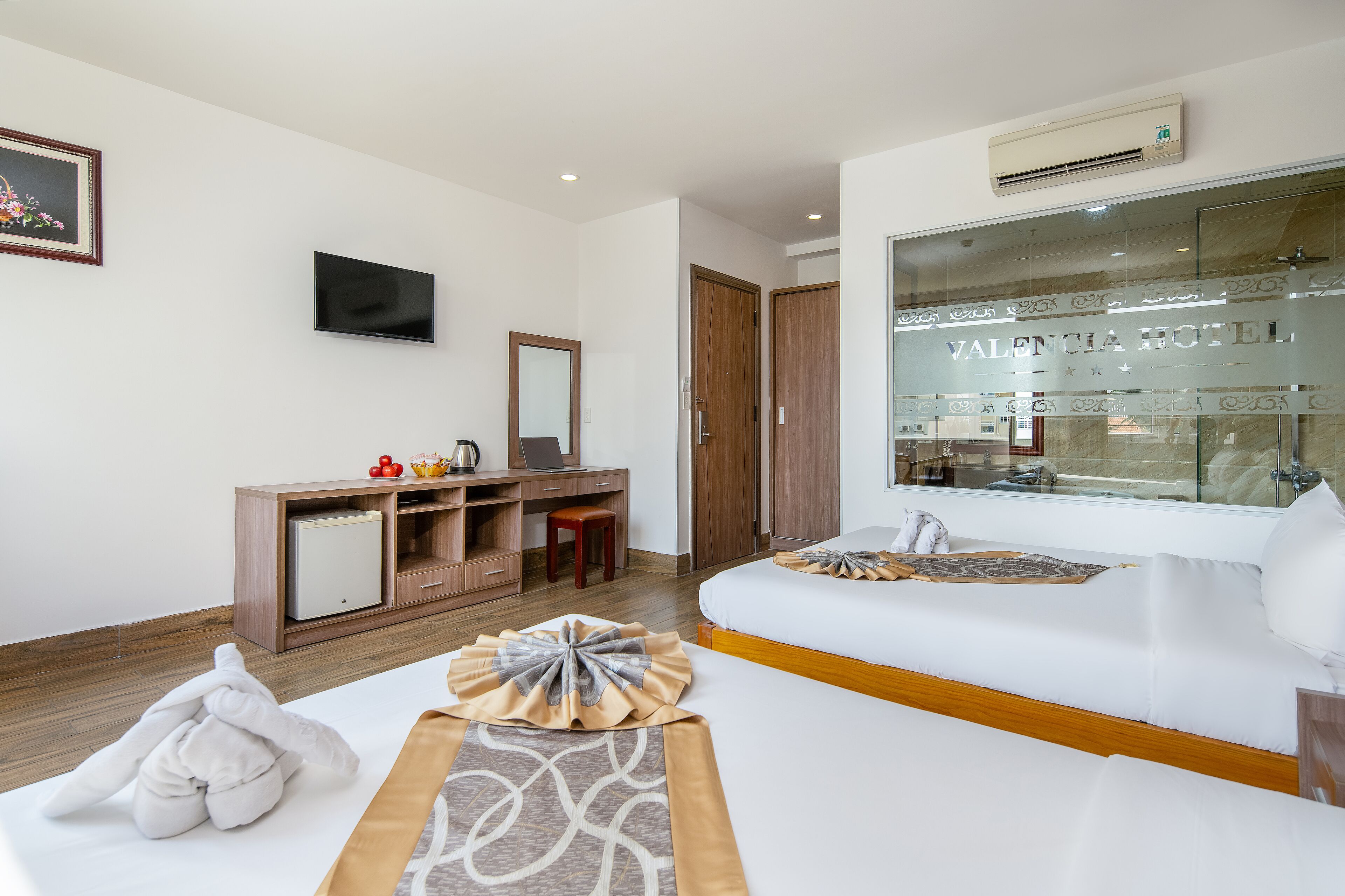 A hotel room with a bed, a desk, a chair, a TV, and a large window with a view of the hotel.