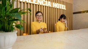 Mostrador de recepción del Hotel Valencia con un panel de madera de fondo y una encimera de mármol.