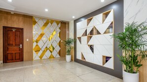 Un vestíbulo con puerta de madera, pared de mármol con diseños geométricos y plantas en macetas.