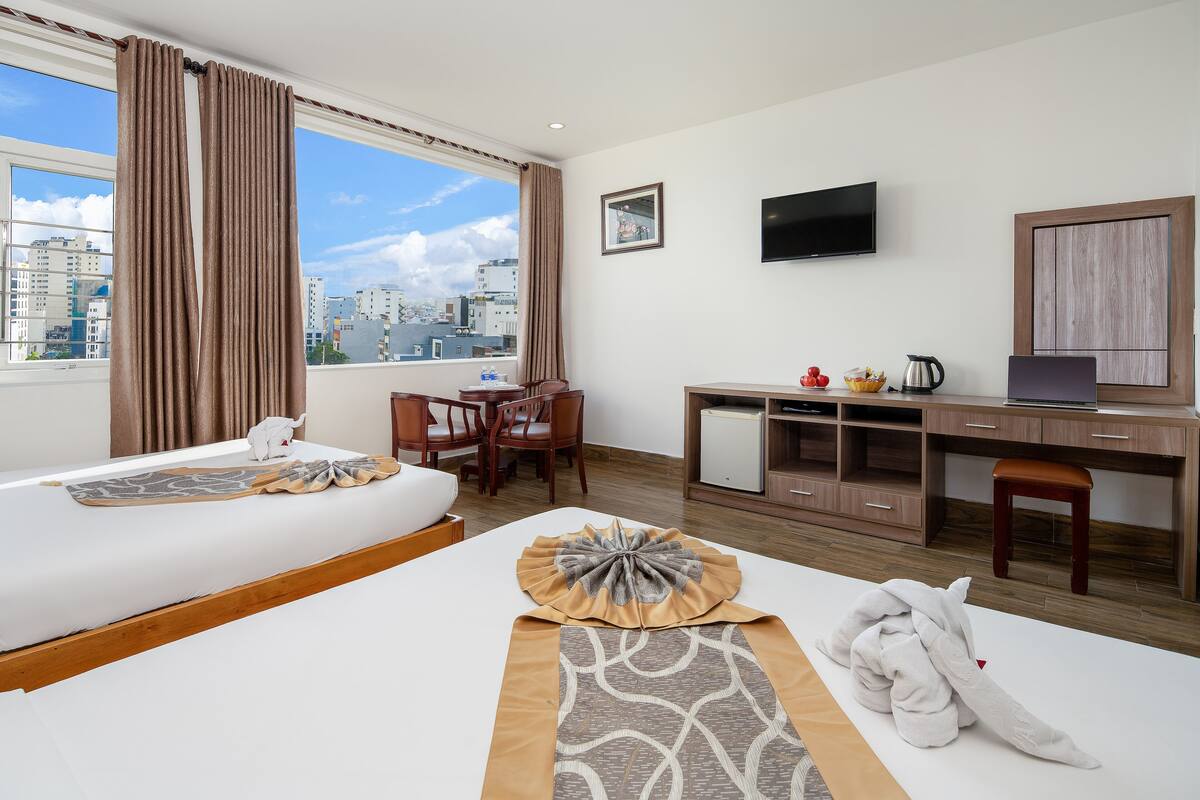 A hotel room with a bed, a desk, a TV, and a view of the city.