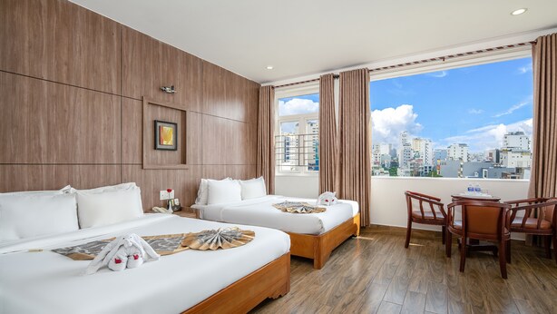 Habitación de hotel con dos camas, zona de comedor y vista a la ciudad.