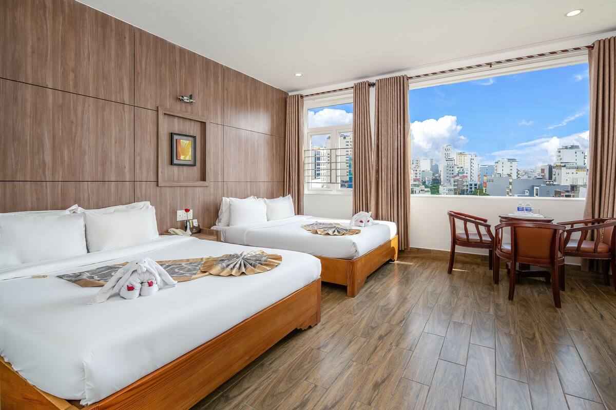 A hotel room with two beds, a dining area, and a city view.