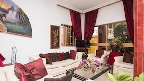 A living room with a sofa, armchairs, a coffee table, a TV, and a painting. - Niagara Inn (Accra)