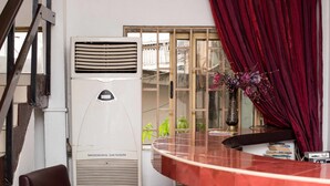 A room with a curved red table, a white air conditioner, a window with a view, and a red curtain. - Niagara Inn (Accra)