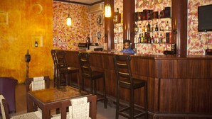 A bar area with wooden bar stools, a counter with a bartender, and a wall with a patterned mural. - Niagara Inn (Accra)